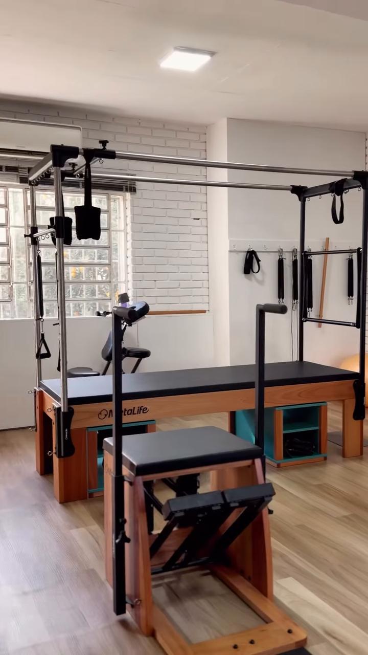 Sala de Pilates inteira: cadillac, chair, espaldar e bolas, paredes de tijolo branco e chão de madeira